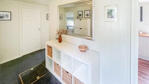 Un couloir avec une console blanche, un miroir, des tableaux encadrés et une porte.