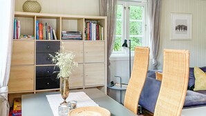 Une pièce avec une bibliothèque en bois, une table à manger agrémentée d’un vase et de salières, et un canapé en osier.