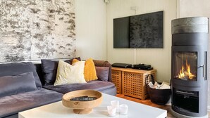 Un salon moderne avec un canapé gris, une table basse en bois, un téléviseur et un poêle à bois.