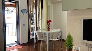 Un salon moderne comprenant un coin repas, un téléviseur fixé au mur et une porte donnant sur un balcon.