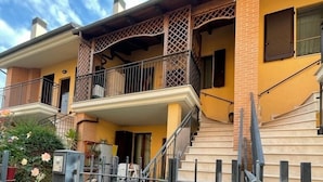 Une maison à deux étages dotée d’un balcon, d’un escalier et d’une entrée fermée par un portail.