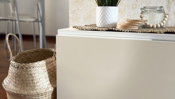 Un salon moderne avec un canapé blanc, un panier en osier, une petite plante en pot et un bocal en verre posé sur un plateau en bois.