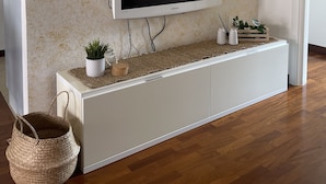 Un salon moderne avec un téléviseur à écran plat fixé sur un meuble blanc, un grand miroir au-dessus du téléviseur et une petite plante posée sur le meuble.