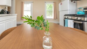 A kitchen with a wooden table, a clear glass vase with a plant, and a stove. - Apartment in town center #1 (West Brookfield)