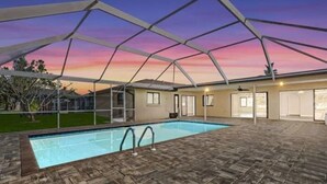 Une piscine avec un patio couvert, un ciel dégagé et une maison en arrière-plan.