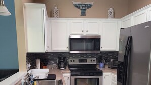 Una cocina moderna con armarios blancos, un refrigerador de acero inoxidable, un microondas, un horno y un lavamanos.