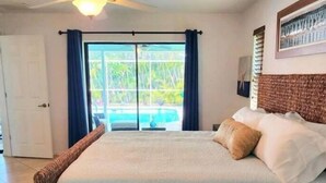 A bedroom with a large bed, a ceiling fan, and a view of a pool through the glass door. - Palm Paradise Poolside (Cape Coral)