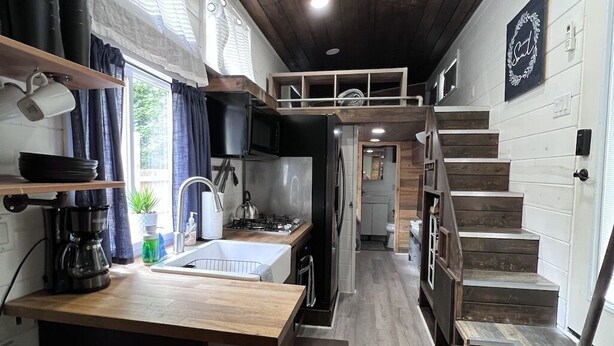 A compact kitchen with wooden countertops, a built-in stove, and a small dining area with stools. - Unique Tiny Home Escape! Fully Equipped & Relaxing, Privacy-Fenced Outdoor Space (Raleigh)