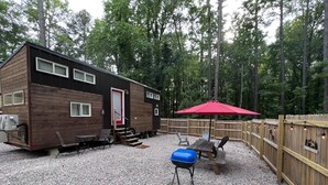 A wooden cabin with a red door, a gravel patio, and a red umbrella. - Unique Tiny Home Escape! Fully Equipped & Relaxing, Privacy-Fenced Outdoor Space (Raleigh)