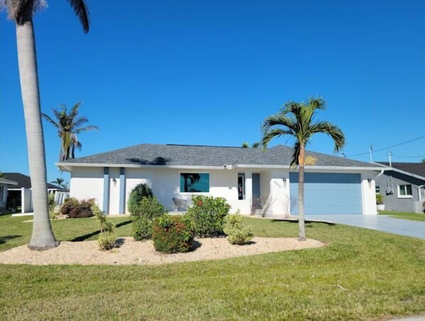 Stroll up to the front entrance of this charming home, surrounded by a lush lawn and palm trees.