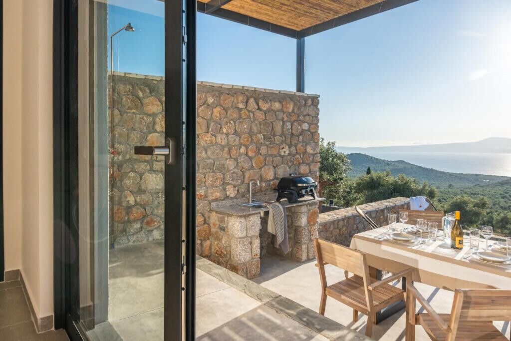 An outdoor dining area with a stone wall, a grill, and a table set for two.