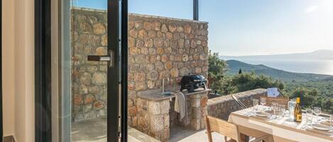 An outdoor dining area with a stone wall, a grill, and a table set for two.