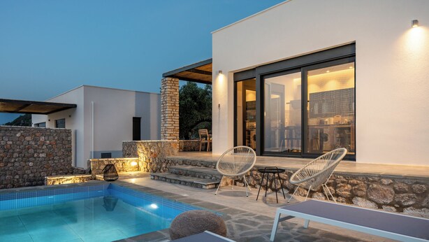 A modern outdoor pool area with stone walls, a glass door leading to a patio, and outdoor seating.