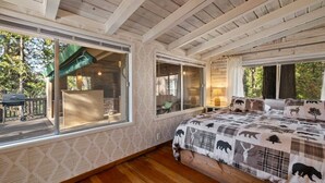 A bedroom with large windows, a wooden ceiling, and a bed with a wildlife-themed blanket. - Walk to town, Lake access, Pet Friendly, King bed (Twain Harte)
