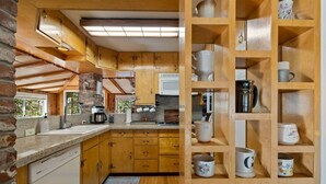 A kitchen with wooden cabinets, a granite countertop, and a built-in shelf with ceramic mugs. - Walk to town, Lake access, Pet Friendly, King bed (Twain Harte)