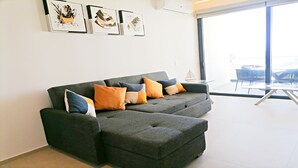 Een moderne woonkamer met een grijze hoekbank, meerdere kussens en drie abstracte kunstwerken aan de muur.