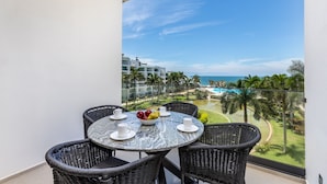 Een balkon met een ronde tafel en vier rieten stoelen, met uitzicht op een zwembad en een golfbaan.