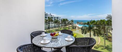 Un balcon avec une table ronde et quatre chaises en osier, donnant sur une piscine et un terrain de golf.