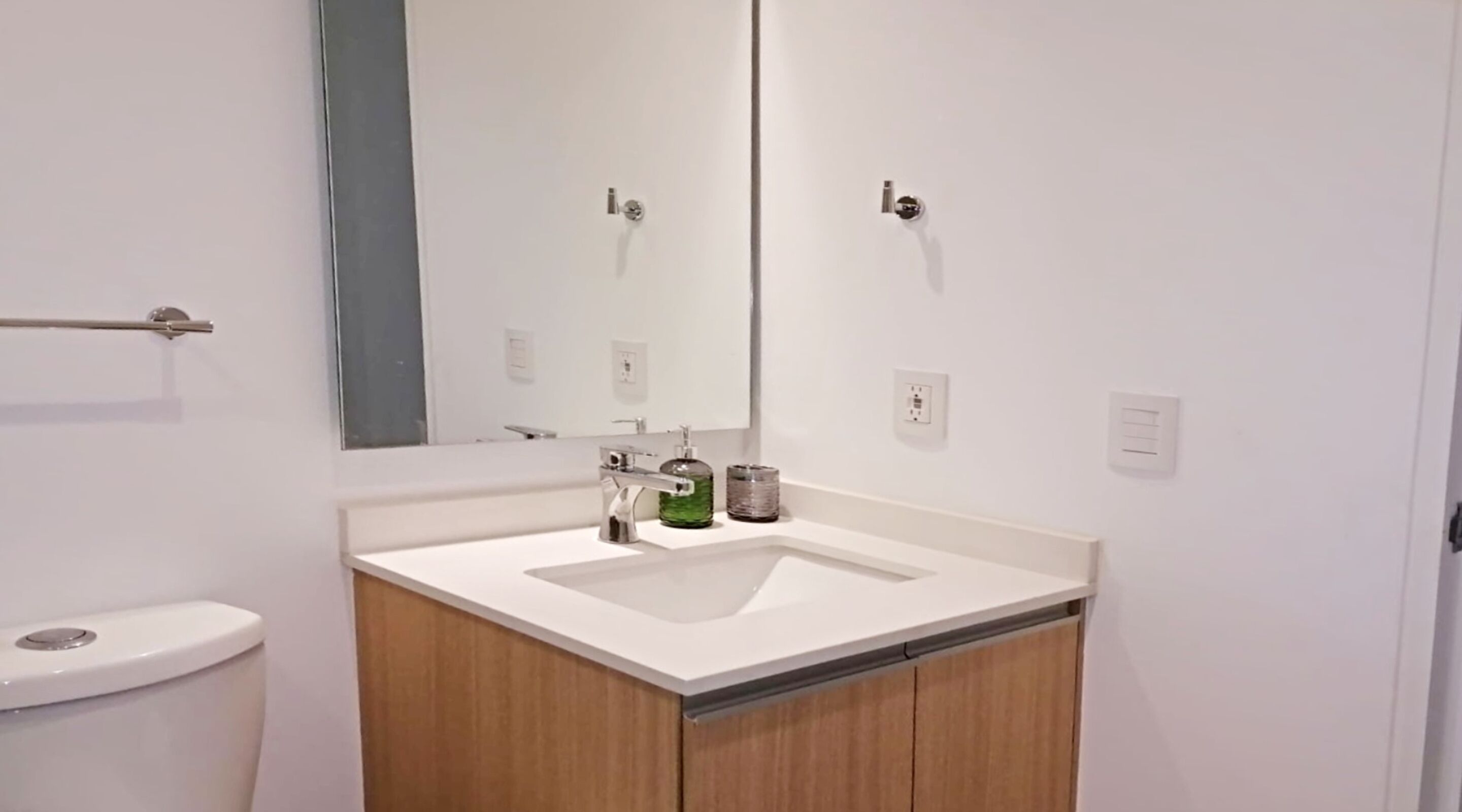 A modern bathroom with a white sink, mirror, and wooden cabinet.