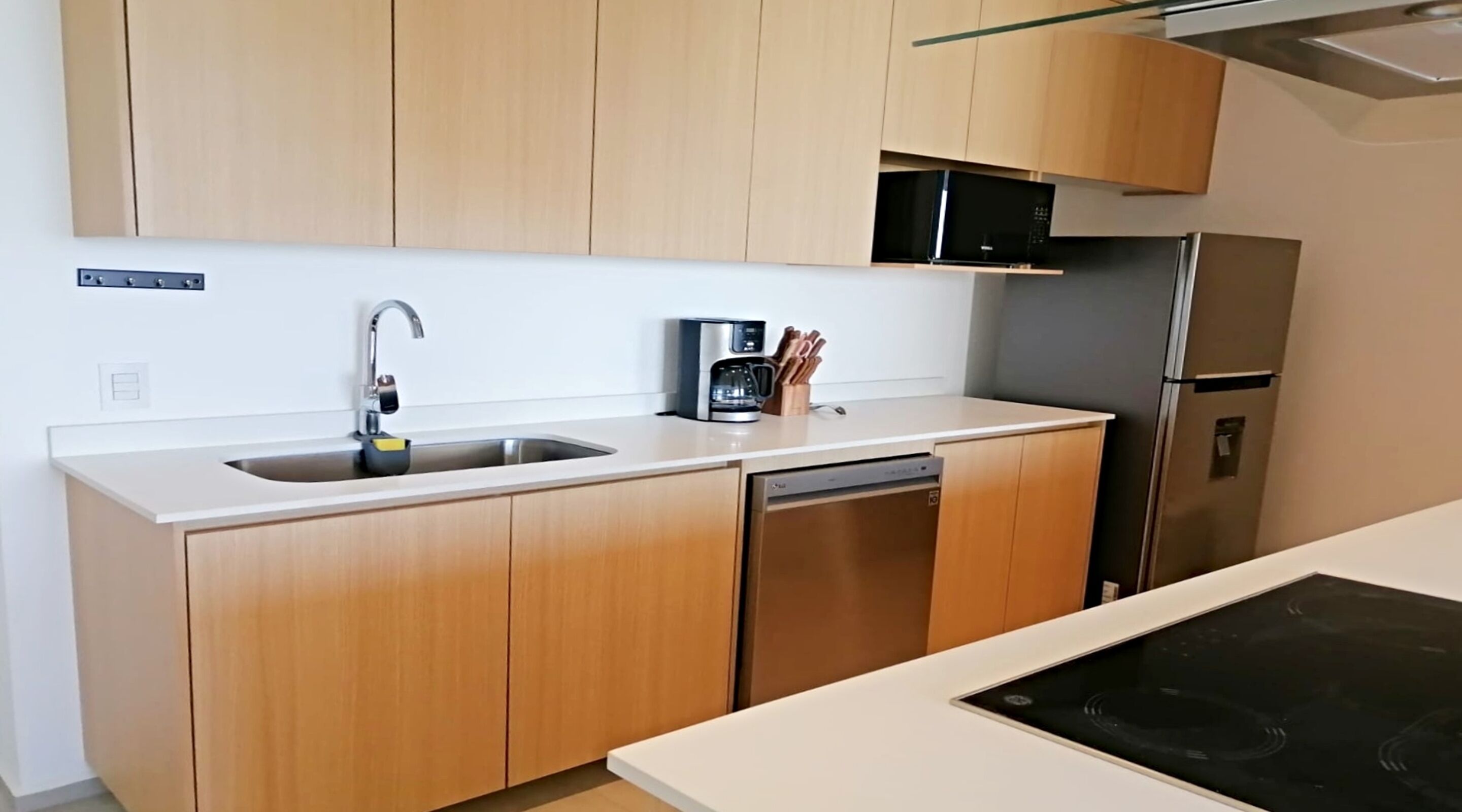 A modern kitchen with wooden cabinets, a stainless steel sink, a coffee maker, and a built-in dishwasher.
