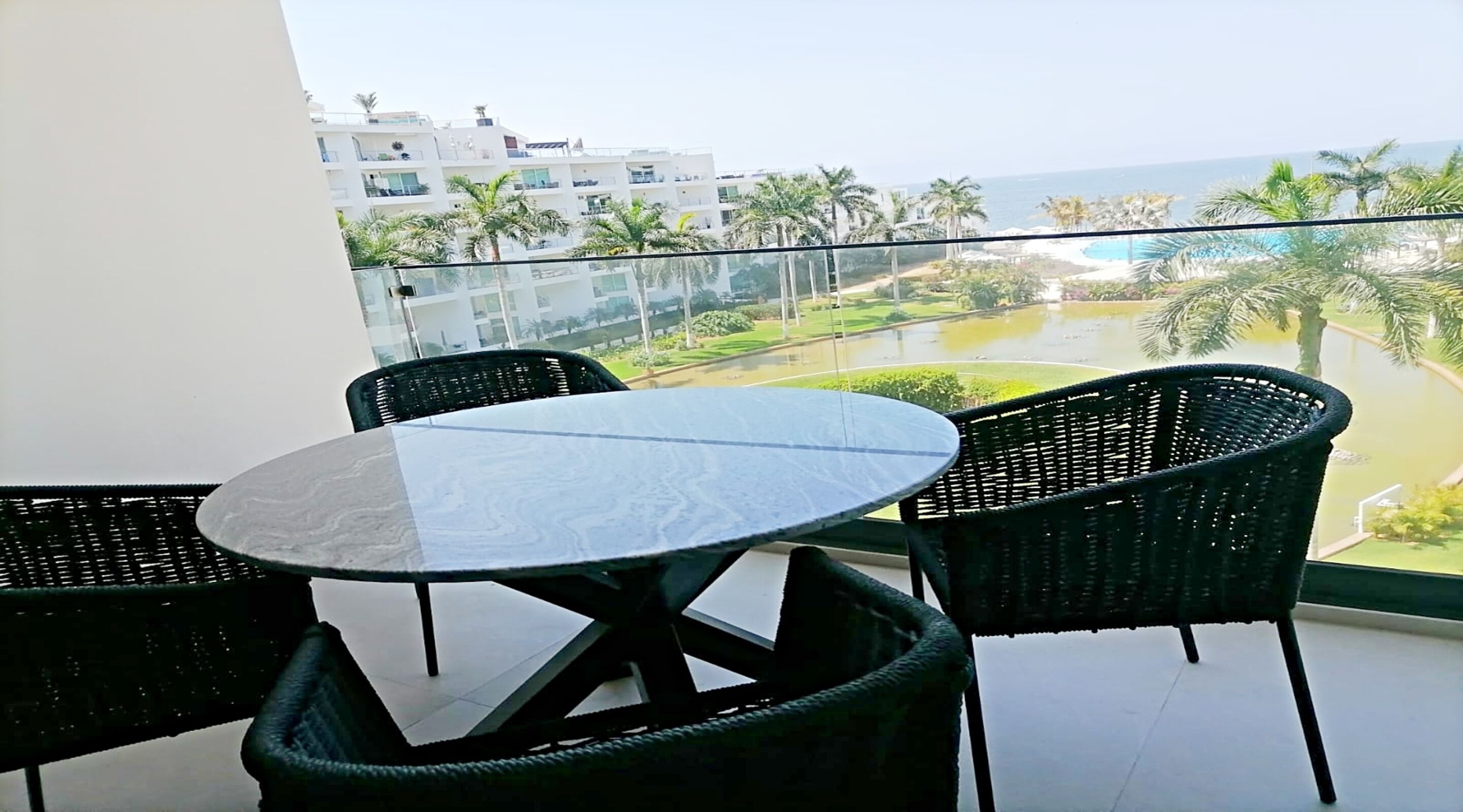 A balcony with a round table and four chairs, overlooking a pool and buildings.