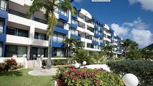 Un hotel de diversos pisos amb balcons, un jardí ben cuidat i un cel serè.