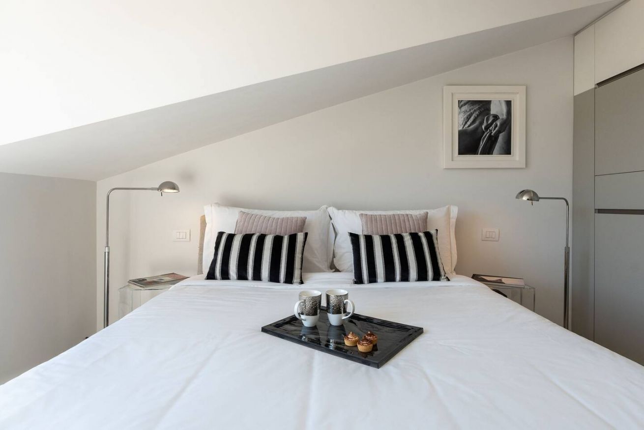 A neatly made bed with a tray of pastries, two bedside lamps, and a framed picture on the wall.