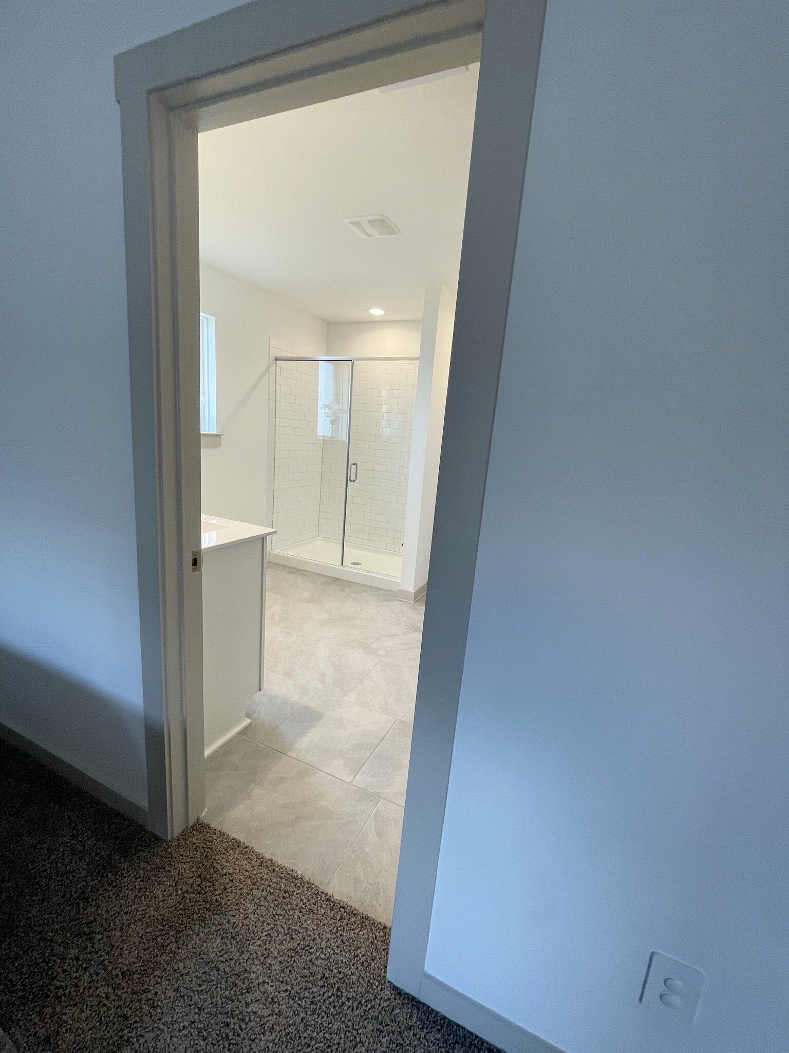 A view into a room with a glass shower enclosure, a white door, and a tiled floor.
