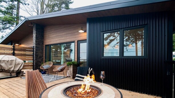 A modern outdoor patio with a circular fire pit, two wicker chairs, and a dining table. - Sea,Sunrises,Sauna | Oceanfront Luxurious Retreat (Campbell River)