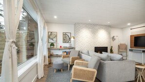 A modern living room with a grey sofa, wicker chairs, a fireplace, and a TV mounted on the wall. - Sea,Sunrises,Sauna | Oceanfront Luxurious Retreat (Campbell River)