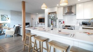 A modern kitchen with white cabinetry, stainless steel appliances, and a central island with stools. - Sea,Sunrises,Sauna | Oceanfront Luxurious Retreat (Campbell River)
