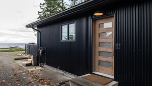 A black metal building with a wooden door, a small porch, and a view of the water. - Sea,Sunrises,Sauna | Oceanfront Luxurious Retreat (Campbell River)