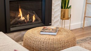 A cozy living room with a fireplace, a woven ottoman, a book, and a potted plant. - Sea,Sunrises,Sauna | Oceanfront Luxurious Retreat (Campbell River)