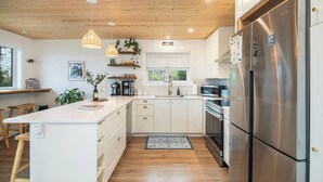 Une cuisine moderne dotée d’un îlot central, d’appareils électroménagers en acier inoxydable, d’un plafond en bois et de luminaires suspendus.
