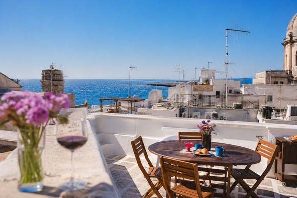 A rooftop terrace with a table set for dining, overlooking a coastal cityscape.