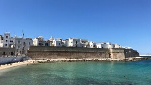 A coastal town with white buildings, a sandy beach, and clear blue waters.