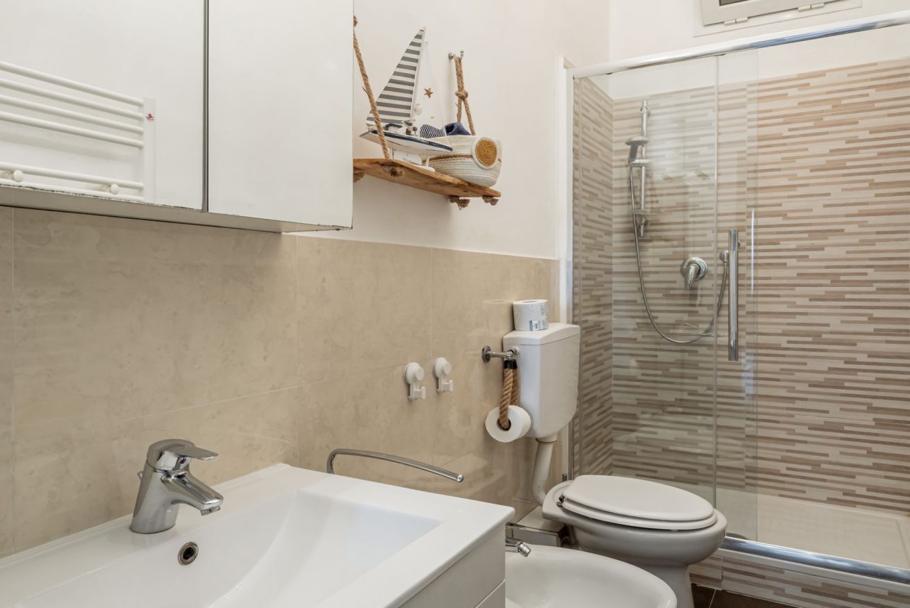 A bathroom with a white sink, a toilet, a glass shower enclosure, and a decorative shelf with a sailboat model.
