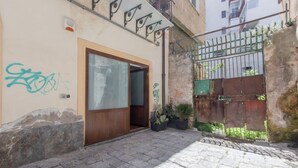 Un edificio con puerta de madera, una reja metálica y un patio empedrado.