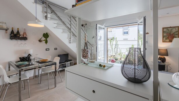 A modern kitchen with a dining area, a staircase, and a large window.