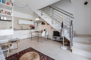 A modern kitchen with white cabinets, a dining area with a glass table, and a staircase with metal railings.