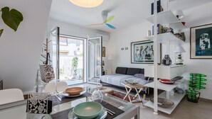 A modern living room with a glass dining table, a sofa, and a white bookshelf.