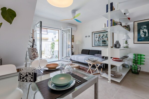 A modern living room with a glass dining table, a sofa, and a white bookshelf.