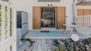 A modern outdoor patio with a dining table, a small garden with cacti, and a sliding glass door leading to a kitchen.