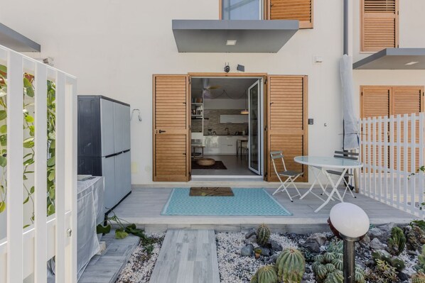 Eine moderne Terrassenanlage mit Esstisch, ein kleiner Garten mit Kakteen und eine Glastür zum Küchenbereich.