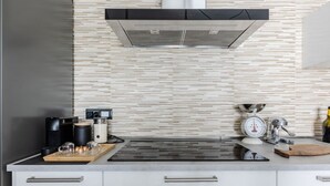 A modern kitchen with a stainless steel range hood, a coffee maker, a scale, and a wooden cutting board.