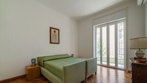 A bedroom with a bed, a nightstand, a lamp, a picture on the wall, and a view through the sliding glass door.