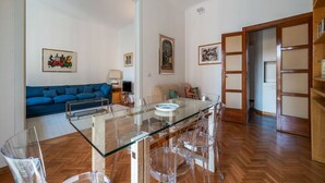 A modern living room with a glass dining table, a sofa, and a bookshelf.