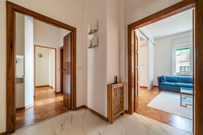 Un couloir avec des portes en bois donnant sur un salon où se trouvent un canapé bleu et un tapis blanc.