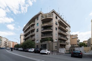 A multi-story residential building with balconies, a gated entrance, and parked cars along the street.