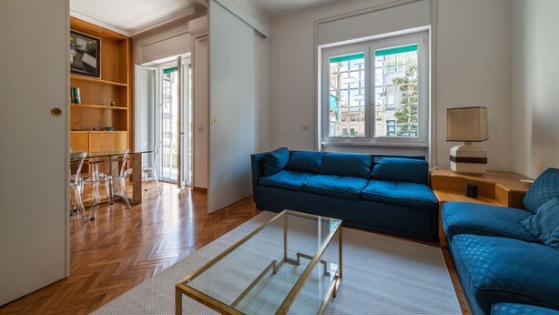 A living room with a blue sofa, a glass coffee table, and a wooden bookshelf.